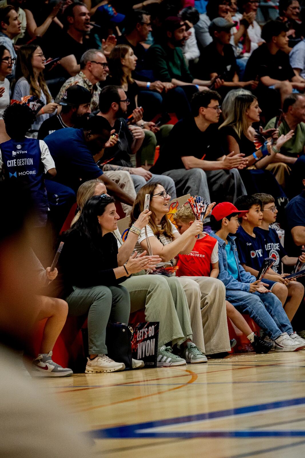 Supportrice filmant le match avec un éventail Let's Go Nyon à la main